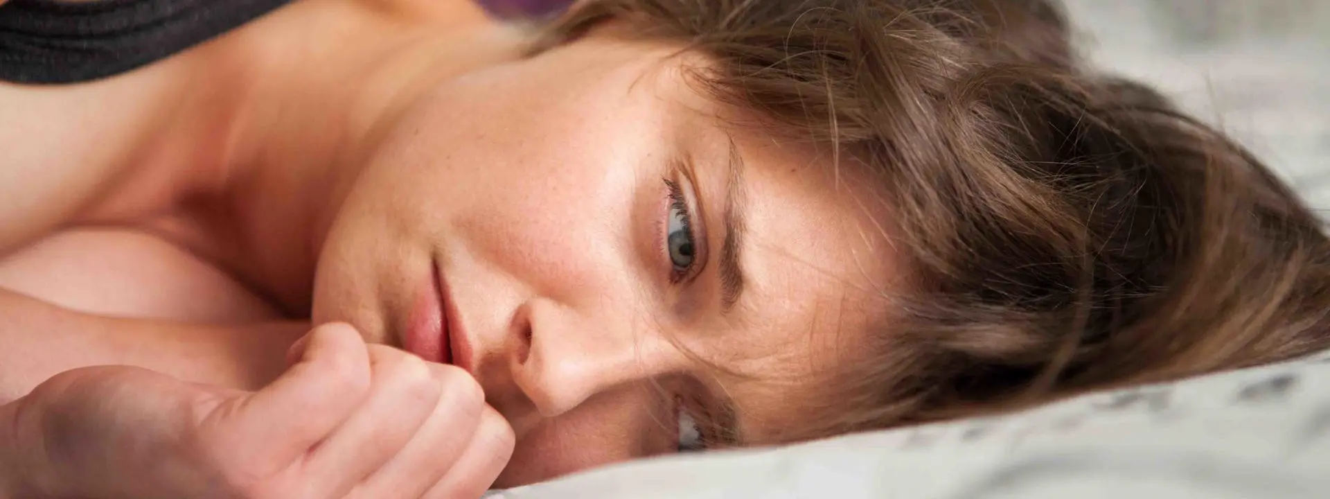 Image shows a woman lying on bed, appearing upset.