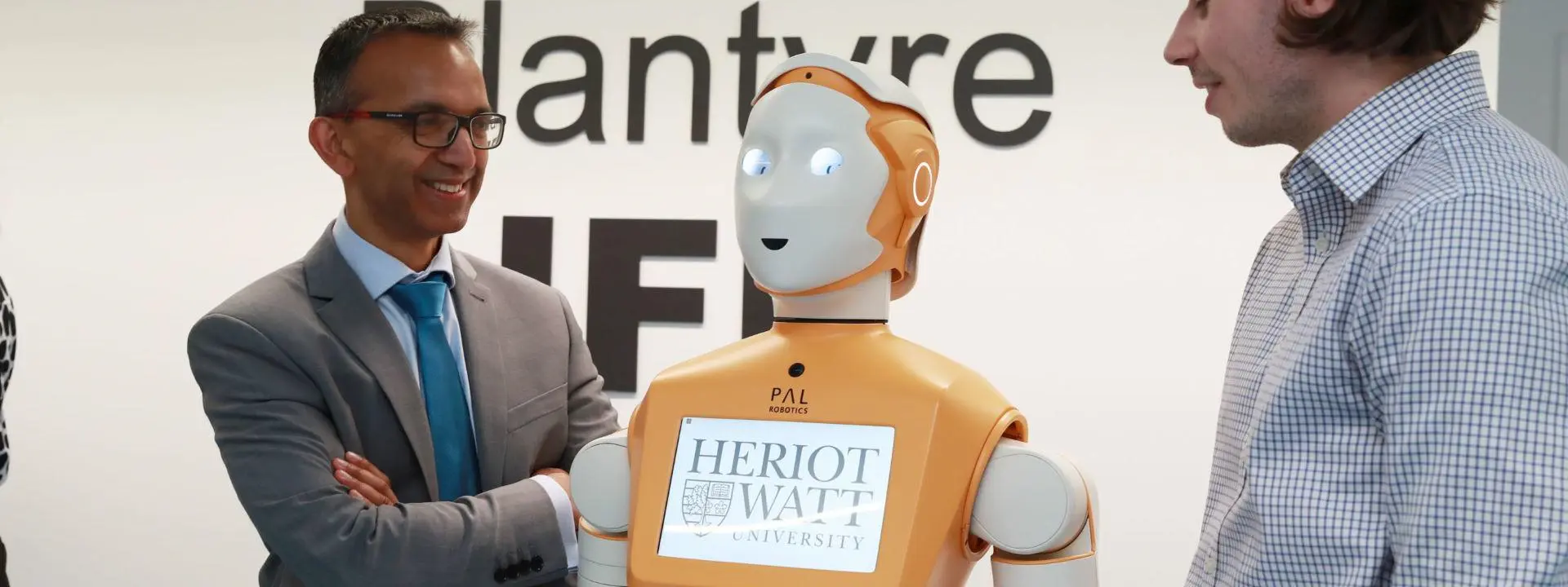 Two individuals standing either side of a humanoid robot named PAL.