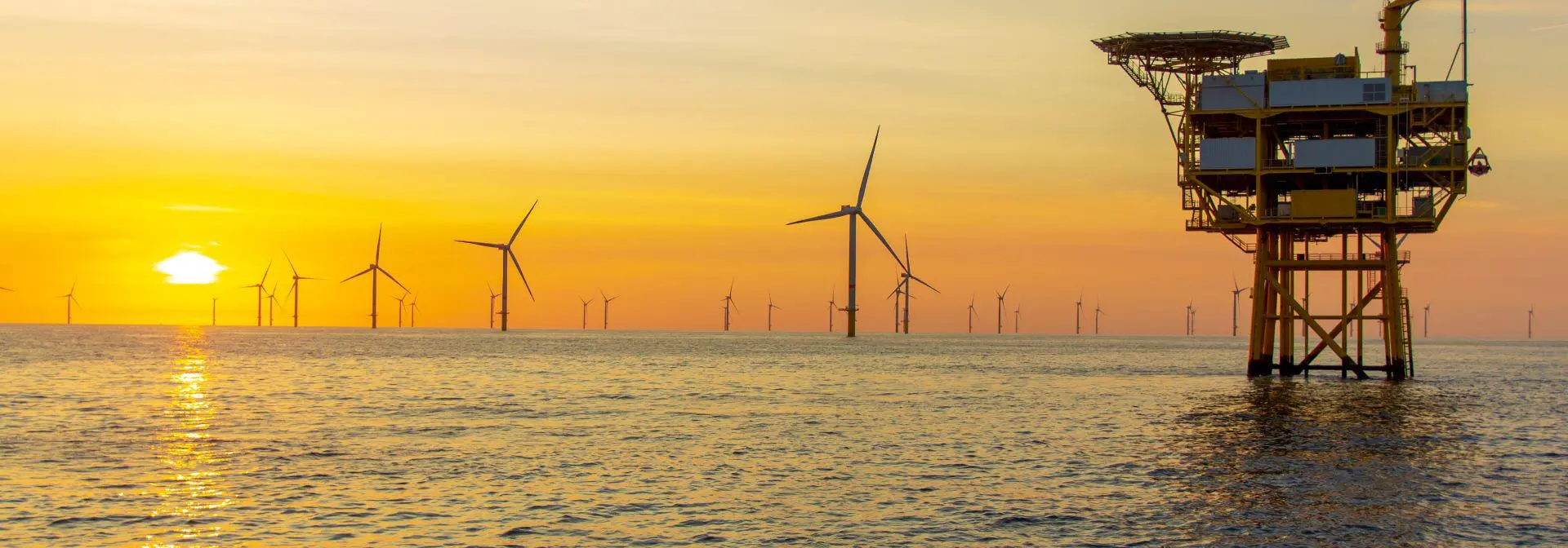 Oil and gas station in open sea with wind farm in background