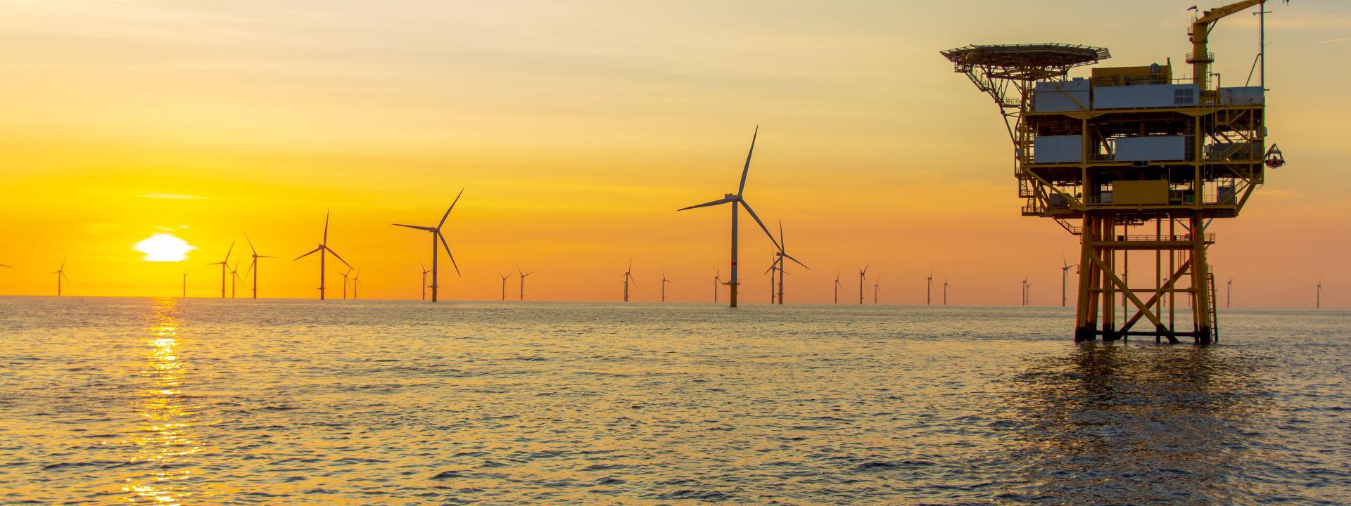The image shows an ocean scene at sunset with an offshore wind farm.