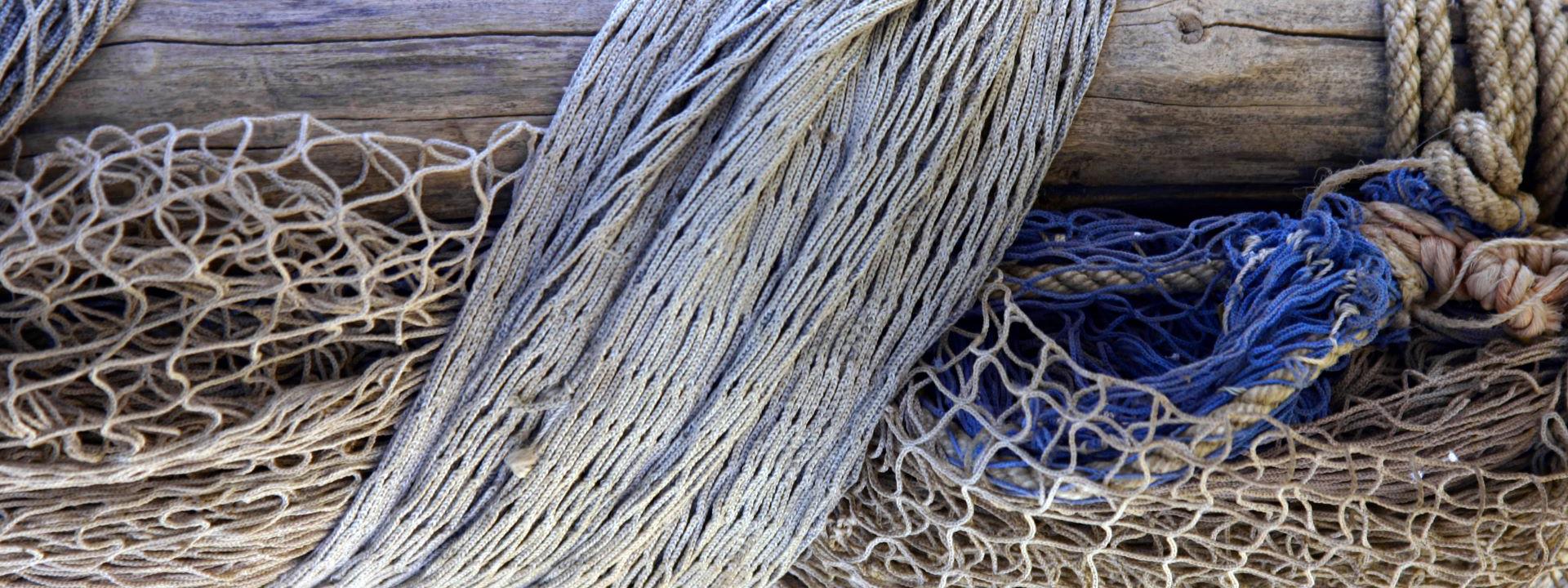 A weathered wooden beam wrapped with various trawling ropes and nets.