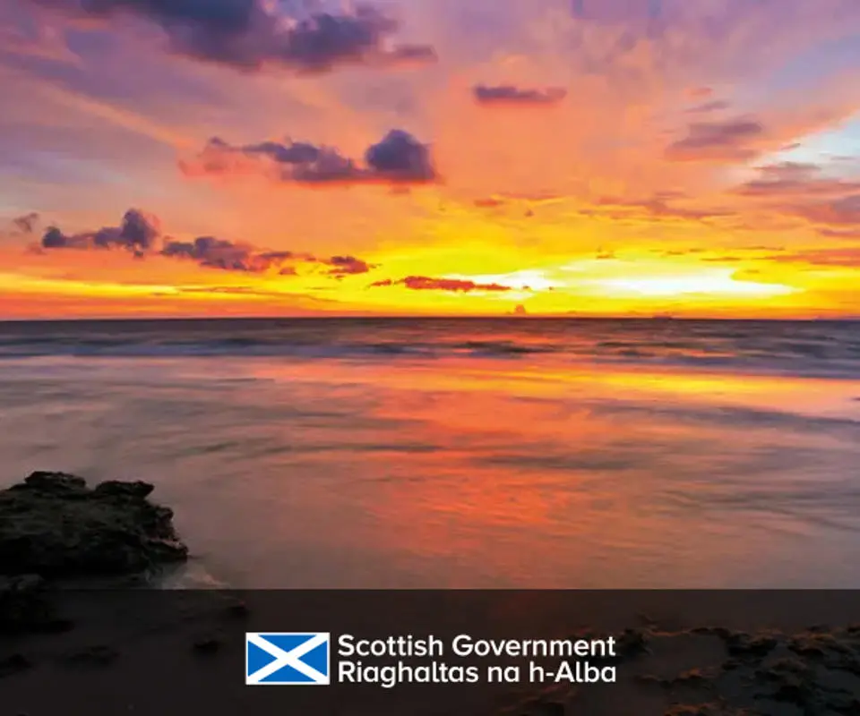 A vibrant sunset paints the sky in hues of orange, pink, and purple above a calm North Sea.