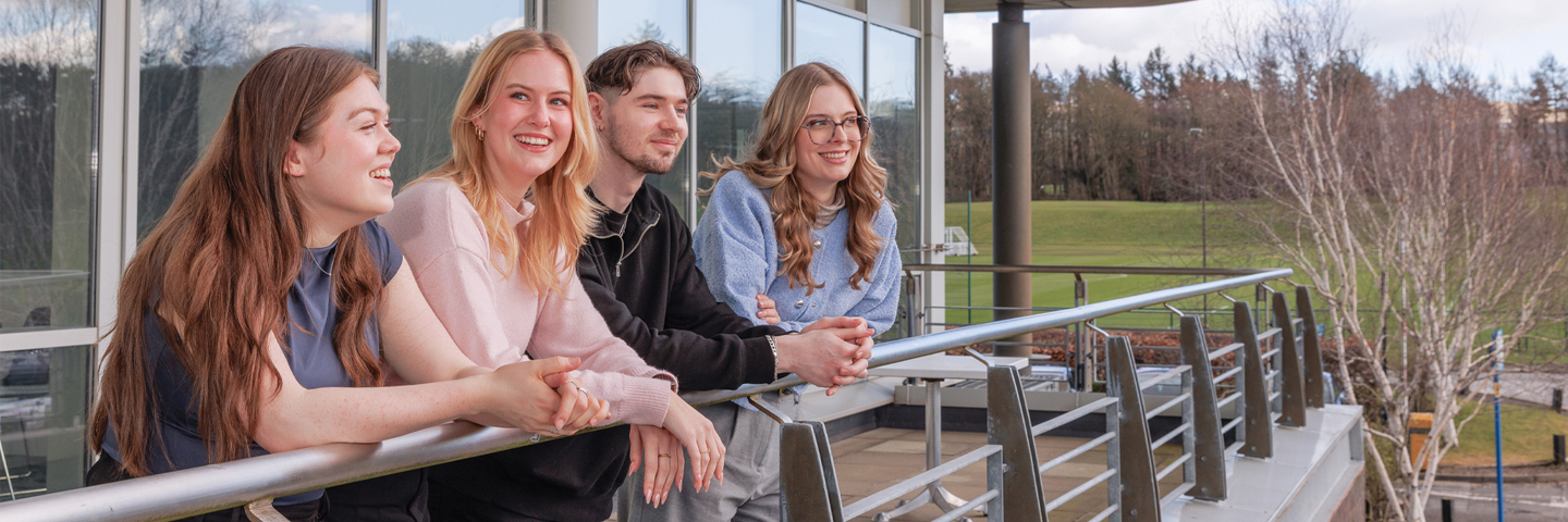Four students casually leaning on the EBS building balcony railing.