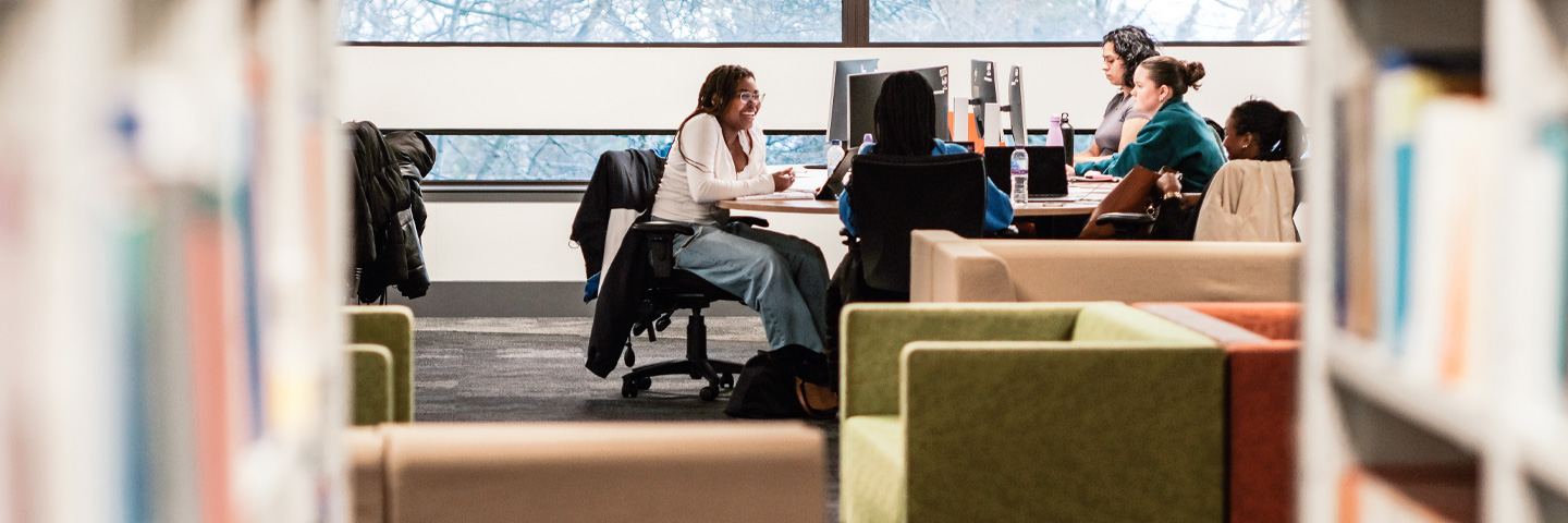 Students seated at tables in the library, engaged in reading and studying quietly.