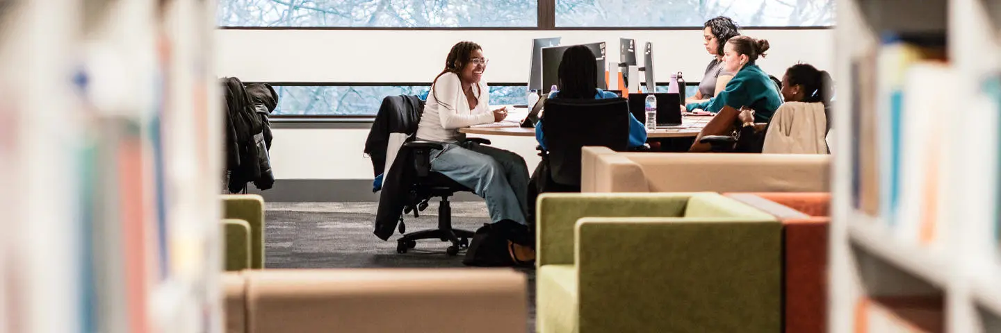 Students seated at tables in the library, engaged in reading and studying quietly.