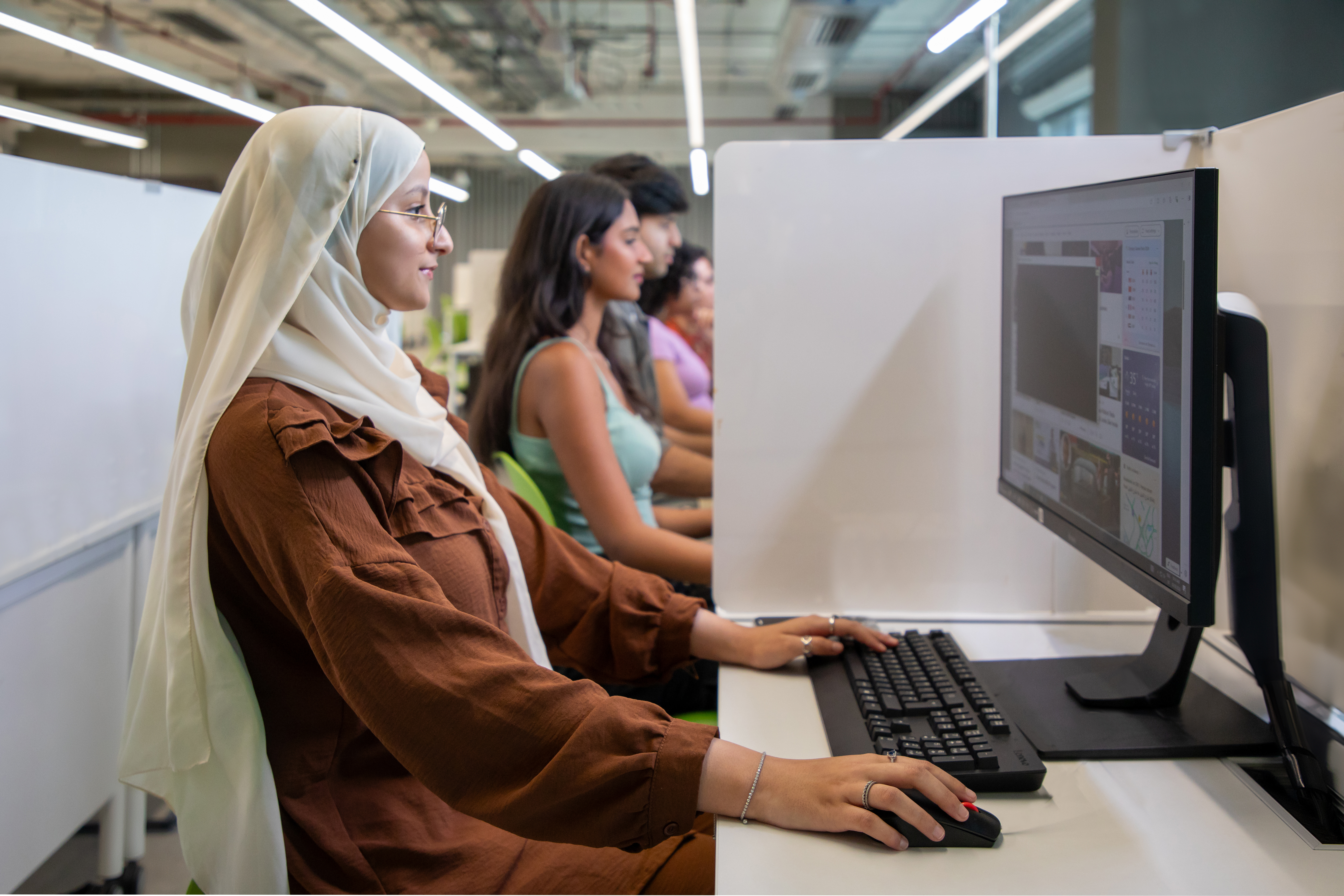 girl in hijab using computer along with other students
