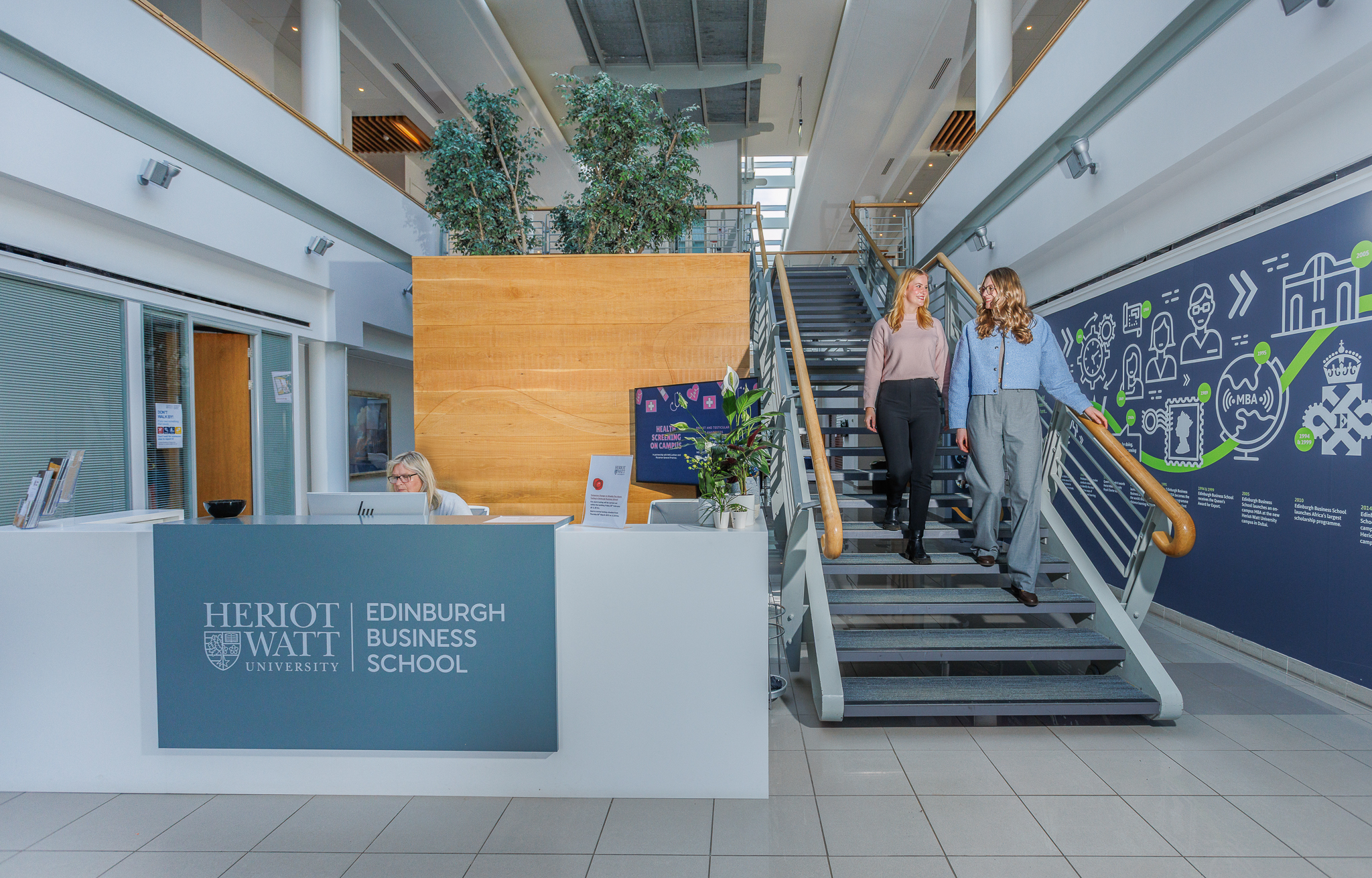 Two students in the Edinburgh Business School walking down the stairs beside reception.
