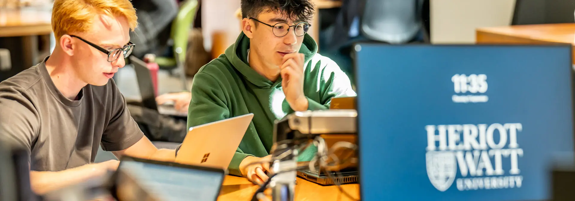 Students working on computer and laptops in common area