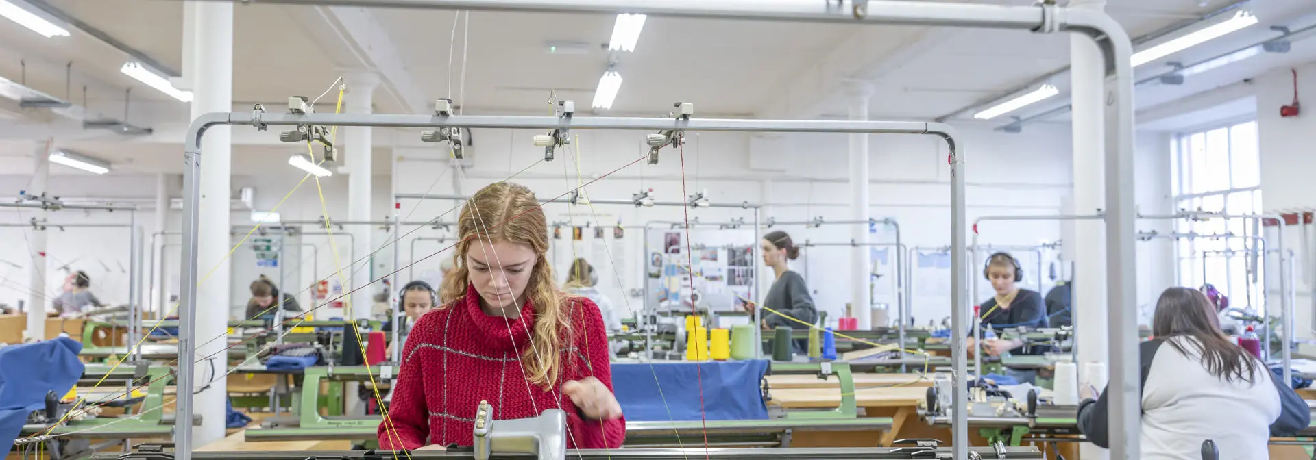 Student working on a knit machine in busy studio.