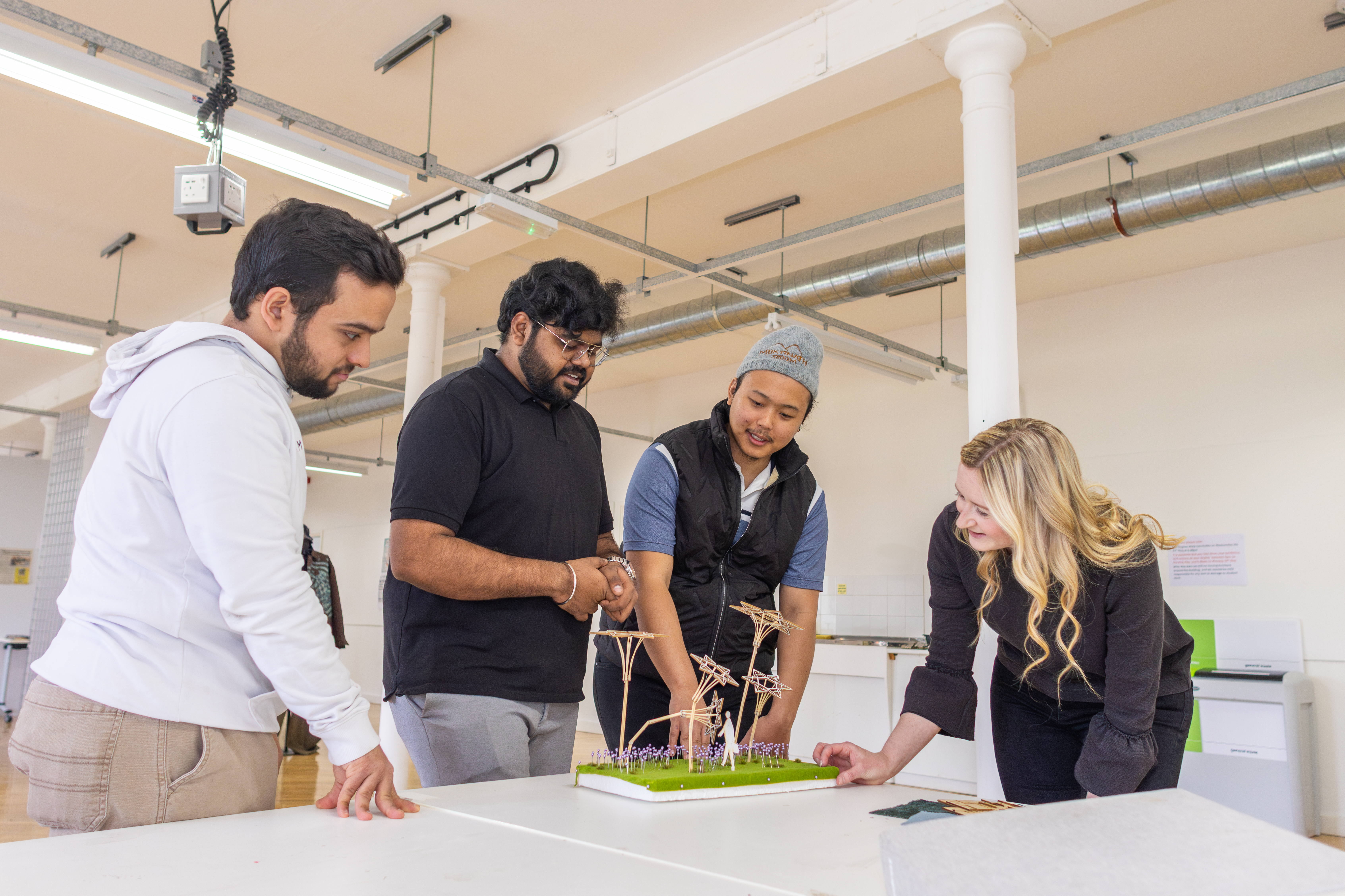 Postgraduate students discuss an intricate model design with an academic in the workspace.