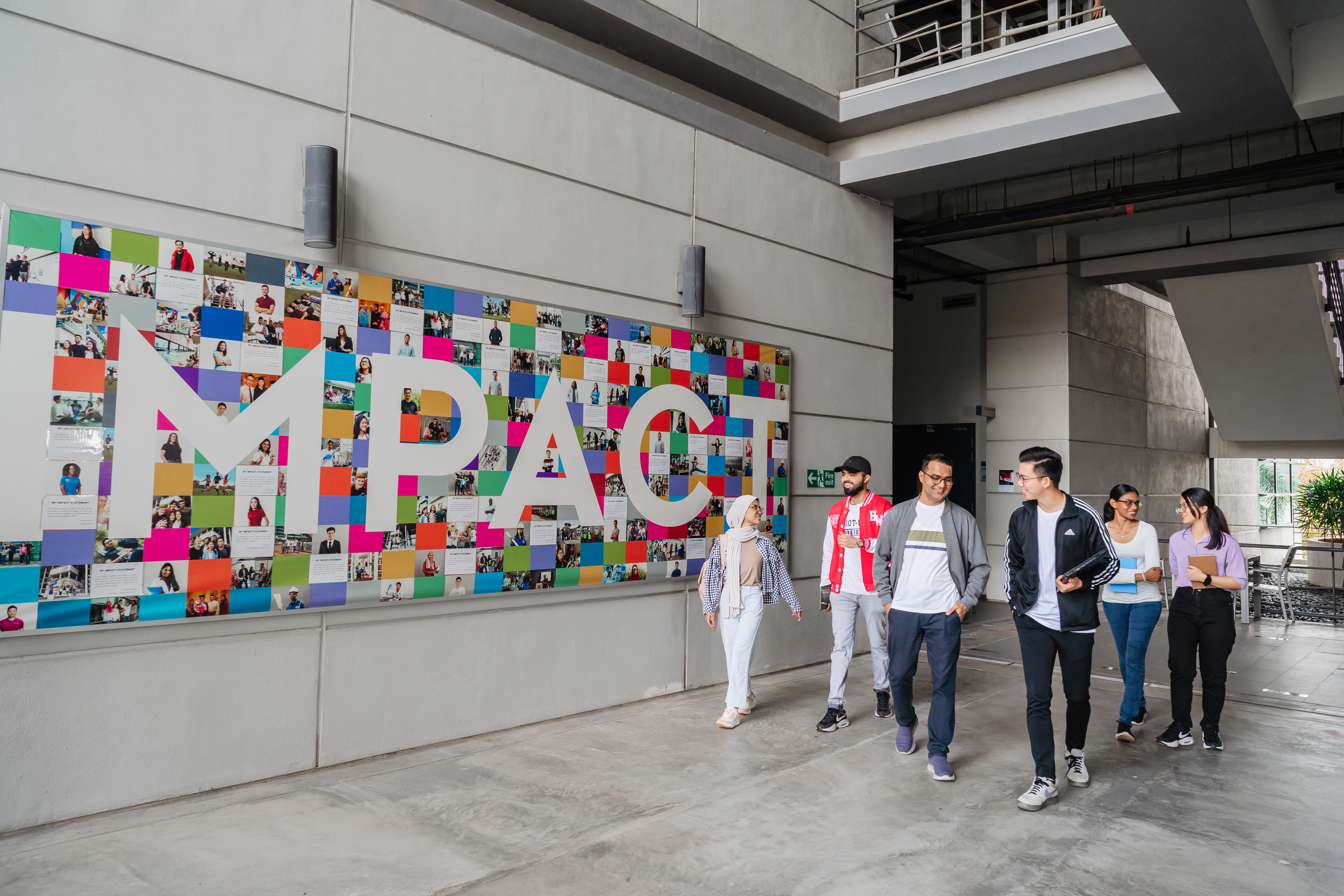 Students walking on campus with impact mural in the background