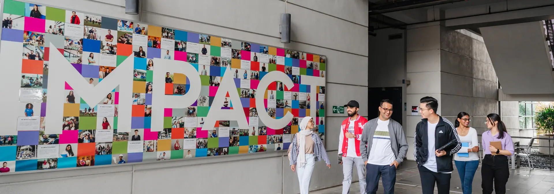Students walking on campus with impact mural in the background