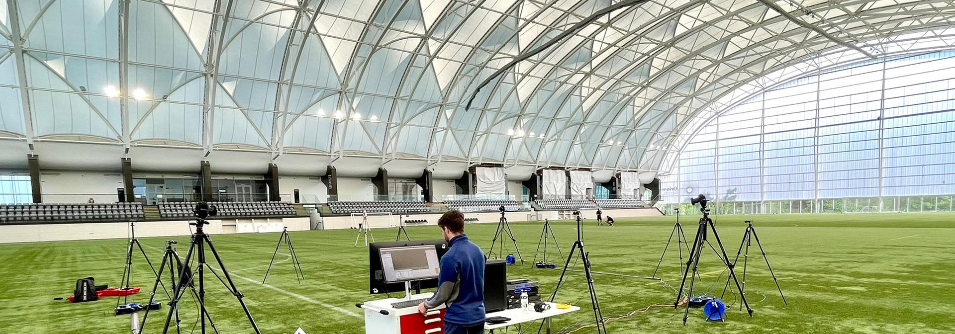 Cameras mounted on tripods as a student uses a computer on an astroturf pitch in the Oriam sports centre.