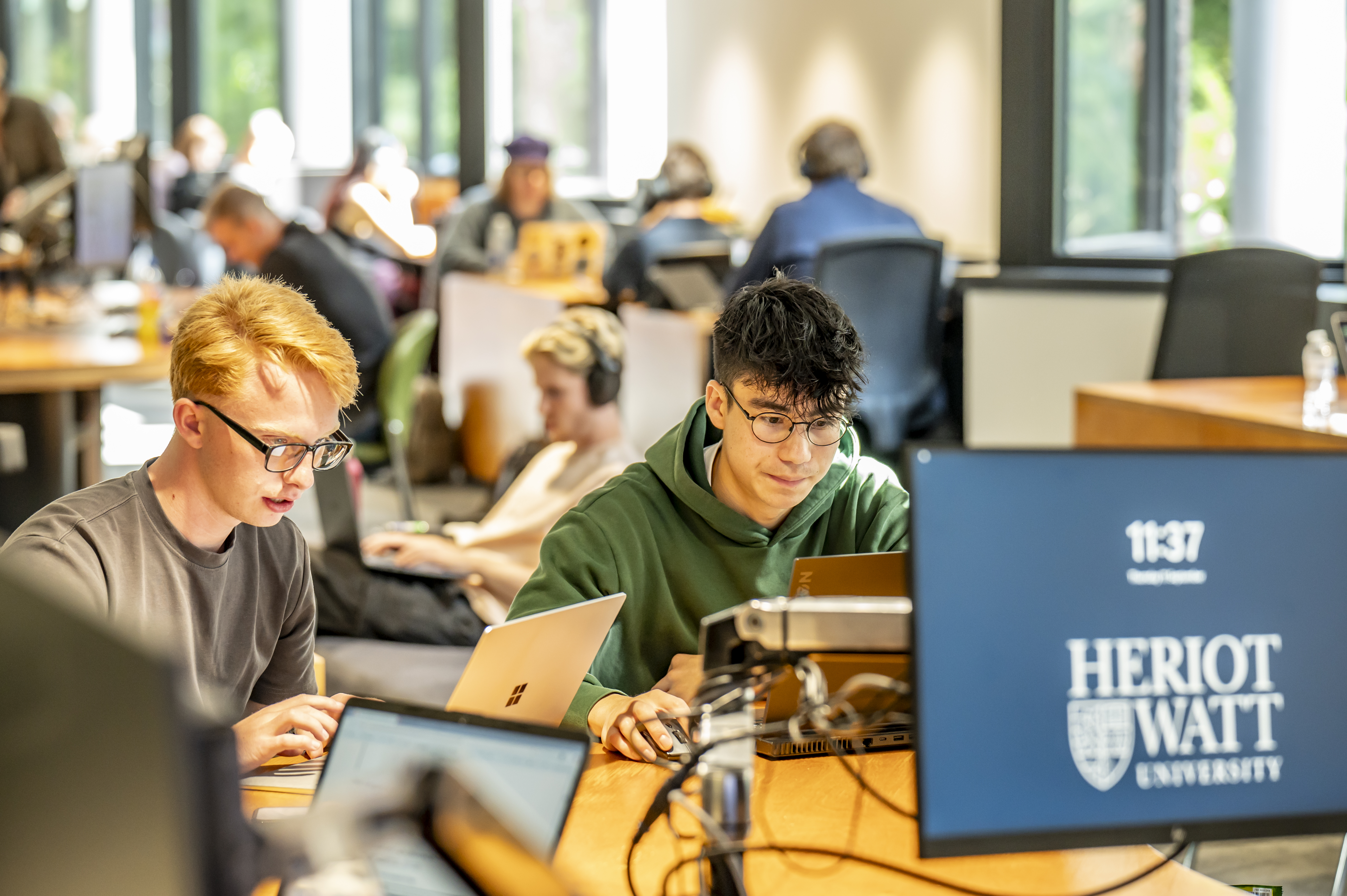 Students working in a shared study space on laptops and computers.
