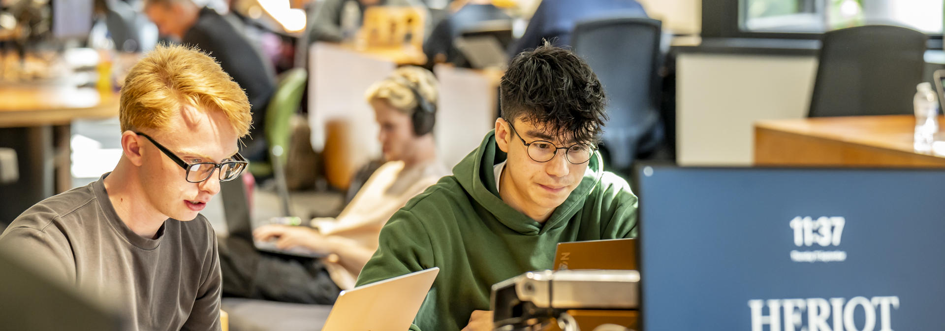 Students working in a shared study space on laptops and computers.