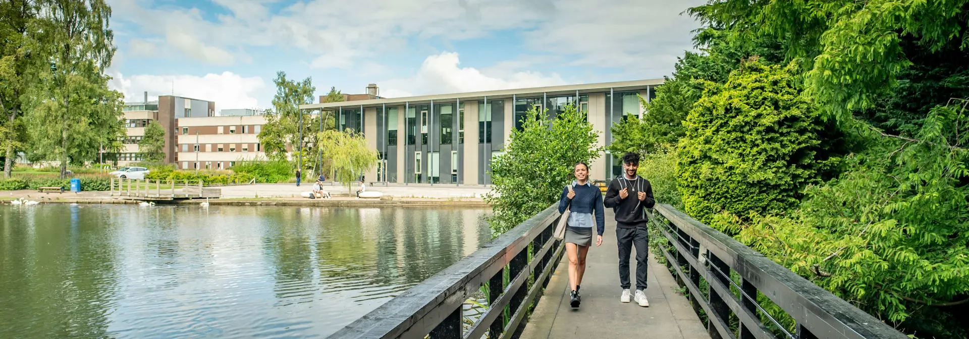 Two students walk across the bridge over the loch with GRID building in the background, Edinburgh Campus.