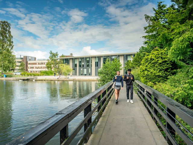 Two students walk across the bridge over the loch with GRID building in the background, Edinburgh Campus.