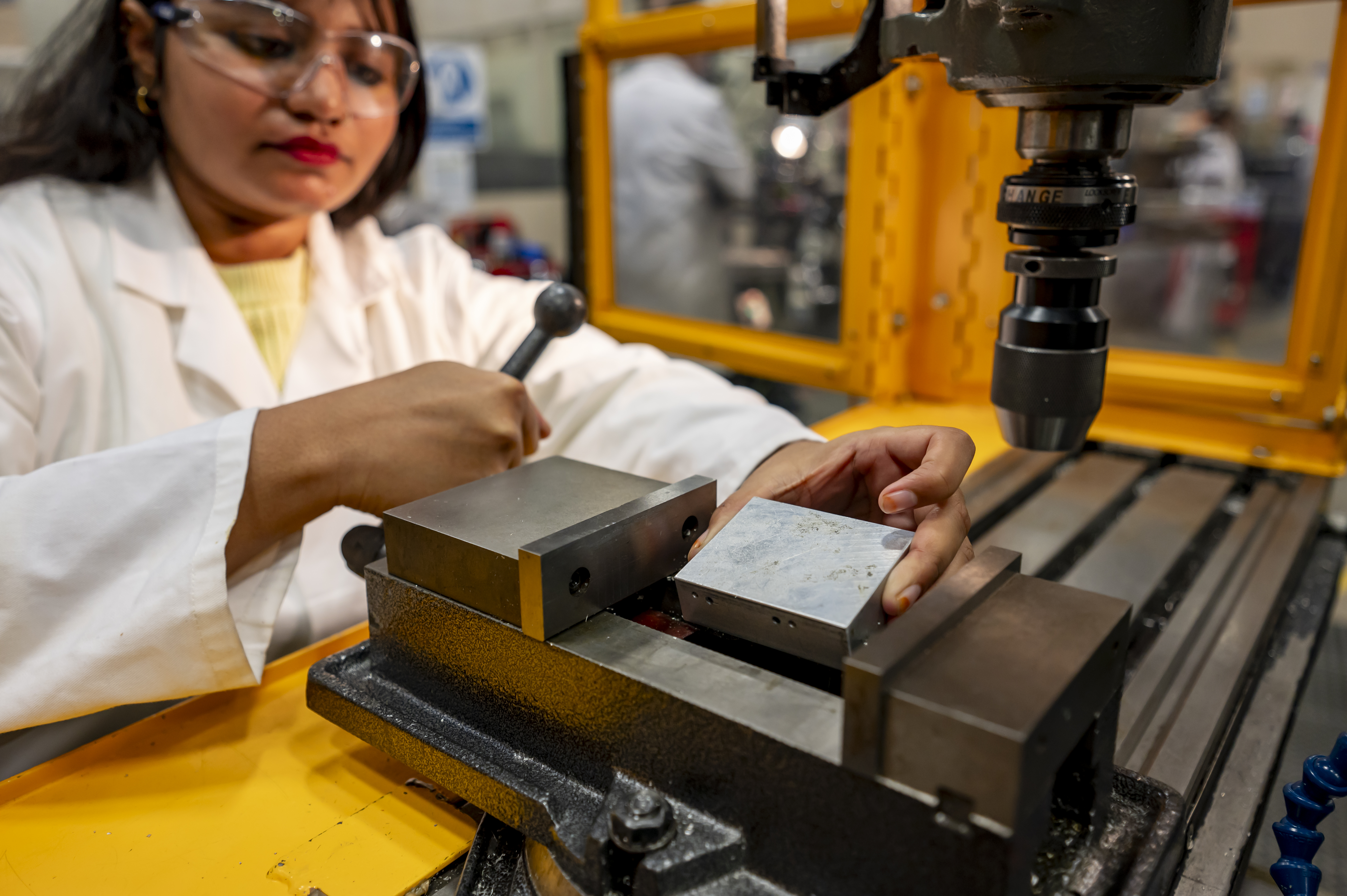Engineering student wearing safety glasses places a piece of metal in a bench vice