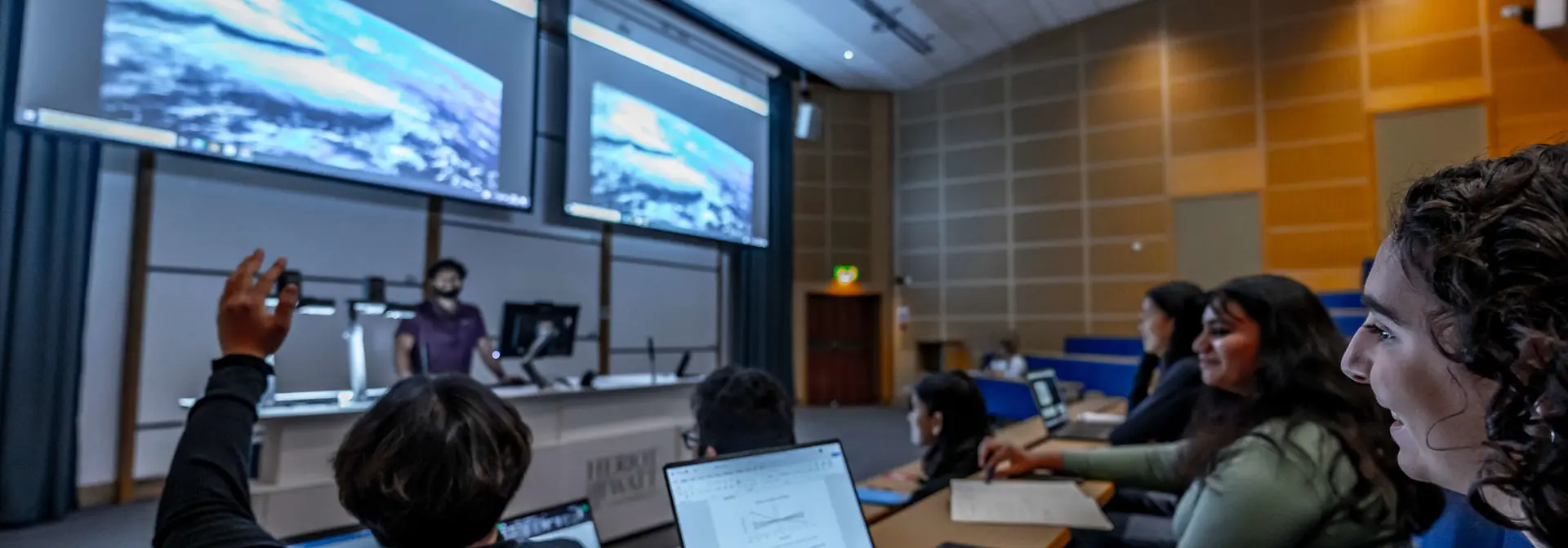 A student holds his hand up in a lecture