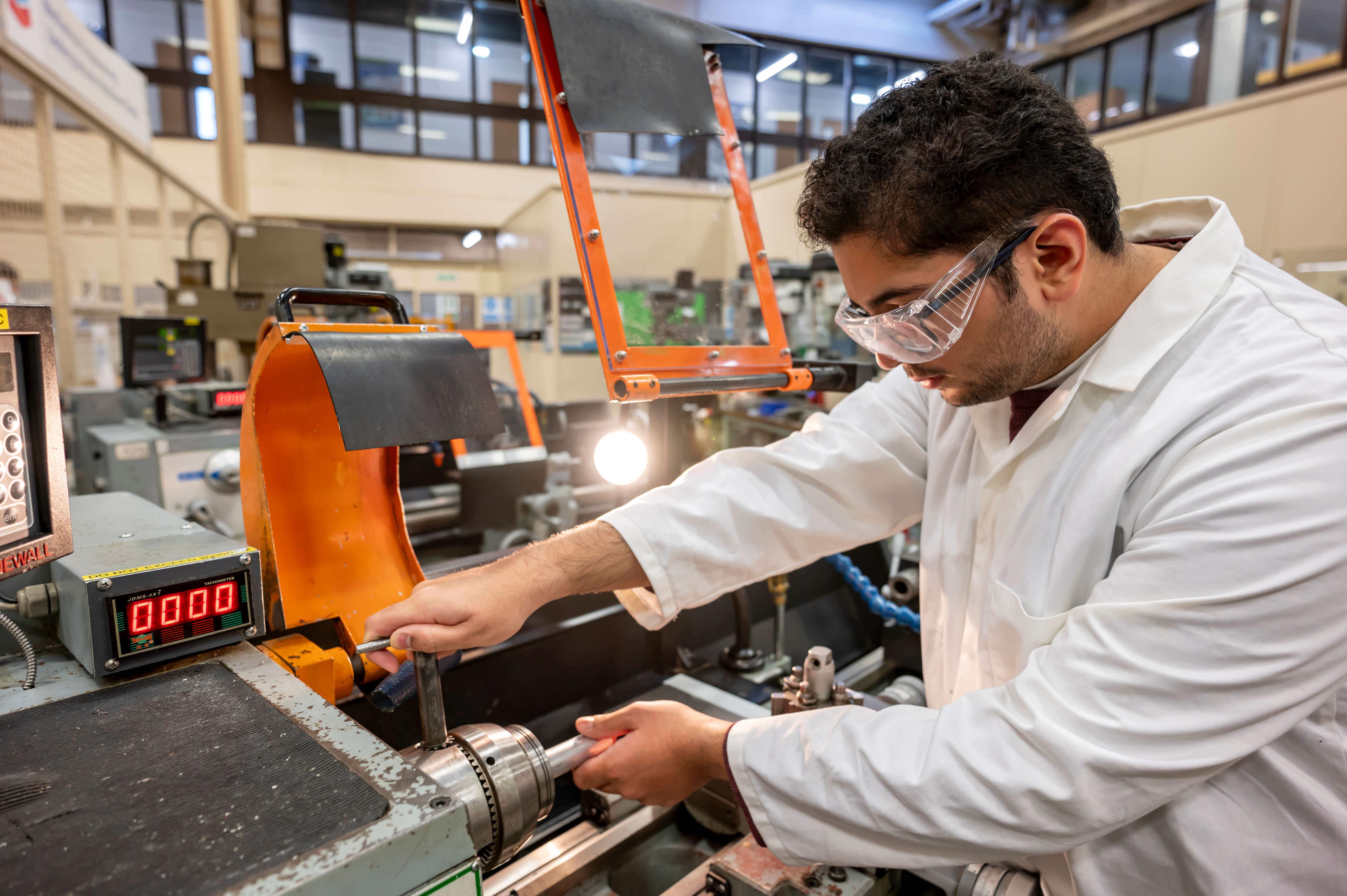 A Mechanical Engineering student in white coat and safety glasses.