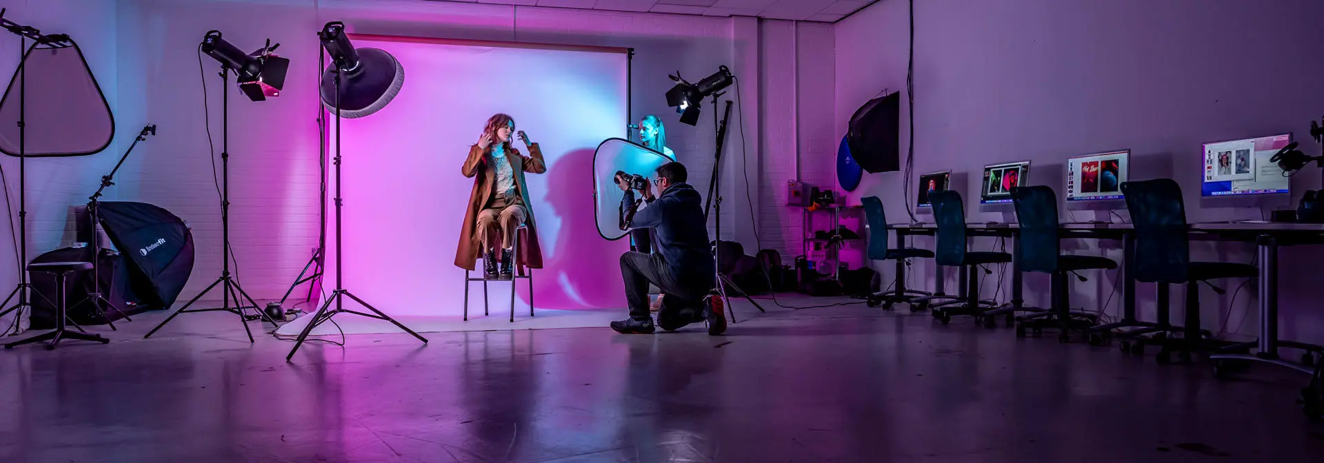 student photographer taking a portrait of model in photography lab with pink and blue lights