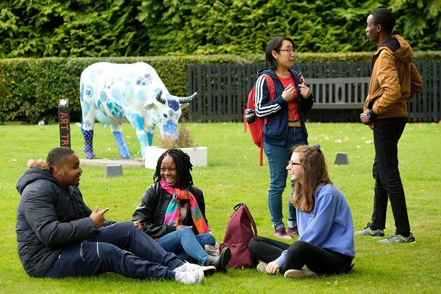 Students sitting on grass beside a statue of a cow 