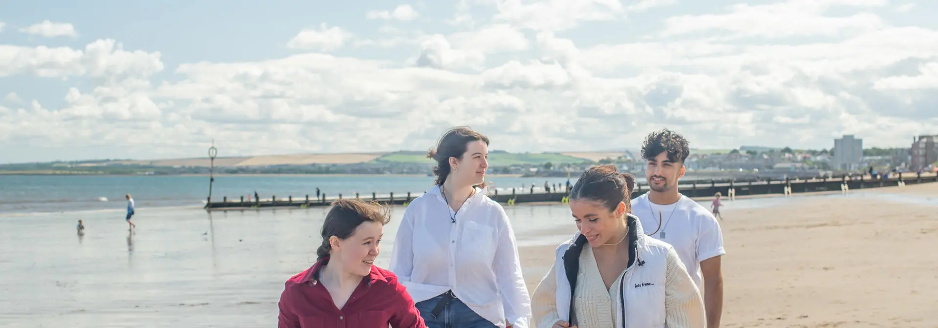 Four individuals walking on a beach on a sunny day.