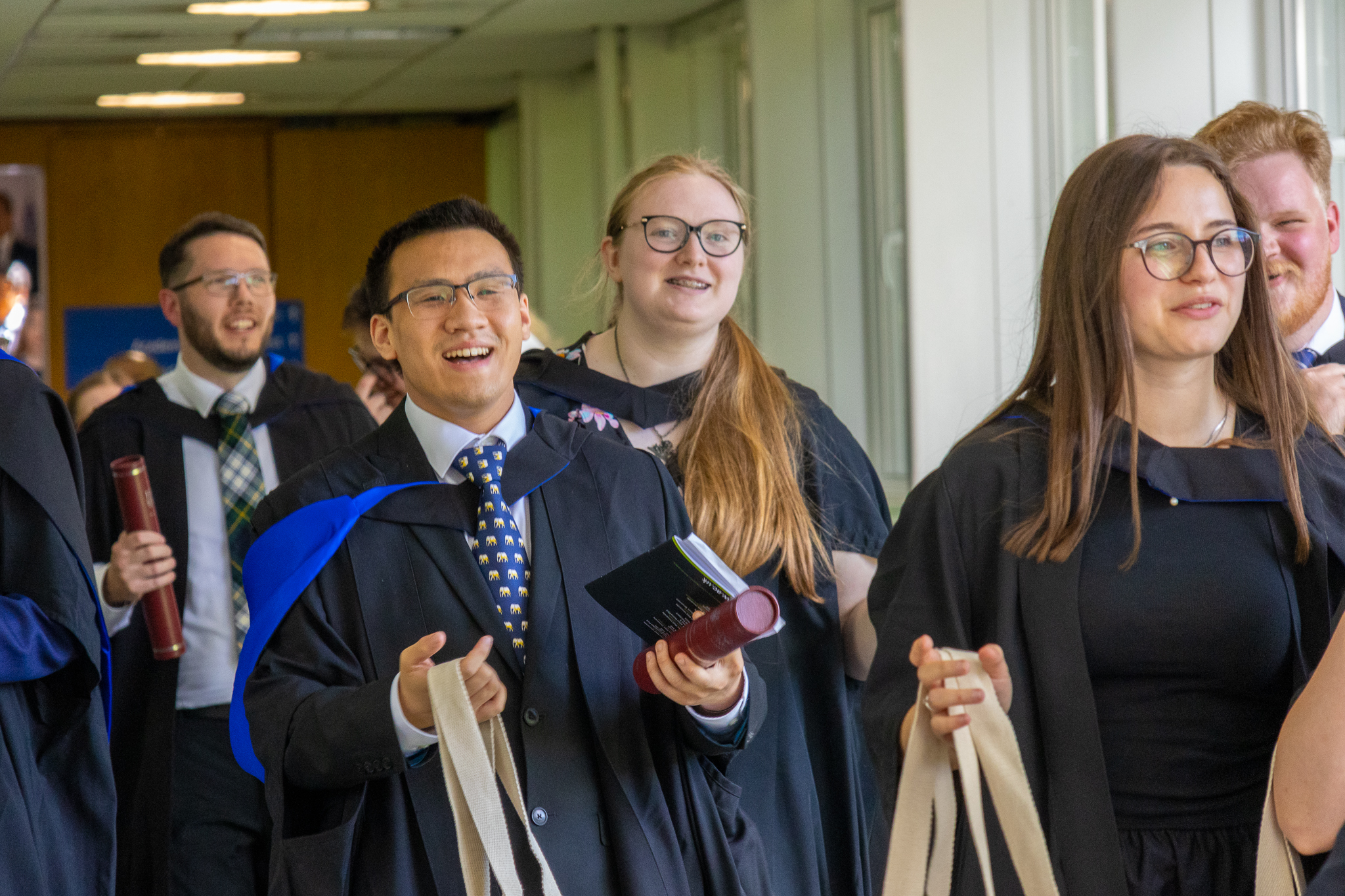 Graduates smiling and walking down the corridor of Edinburgh campus.