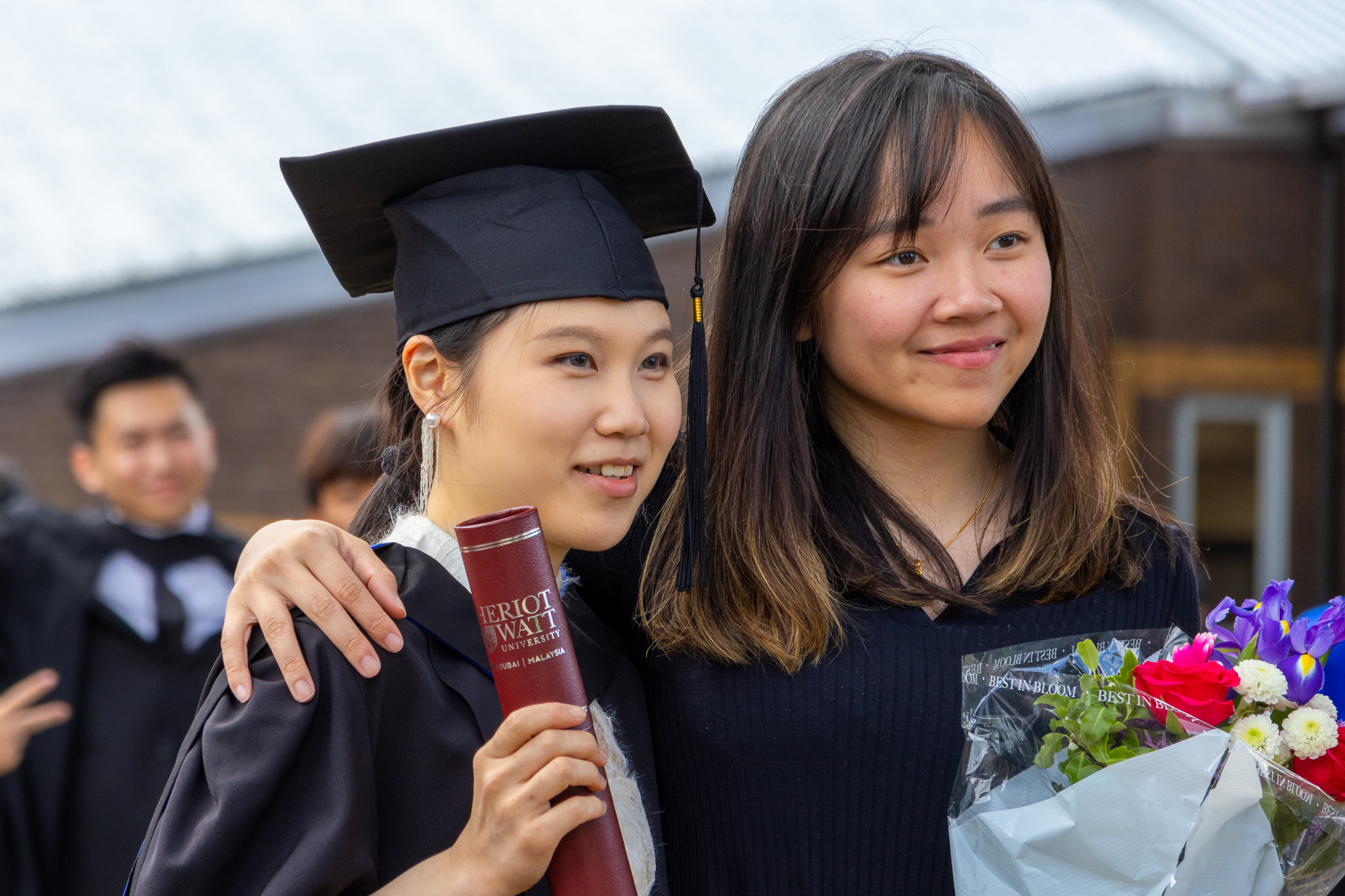 Two graduates at our Edinburgh campus posing with flowers and a certificate holder.