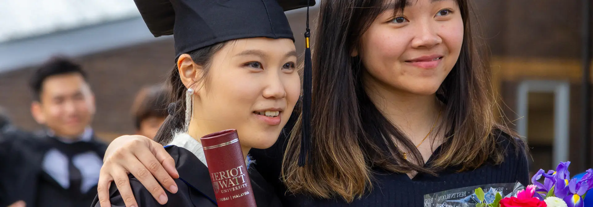 Two graduates at our Edinburgh campus posing with flowers and a certificate holder.