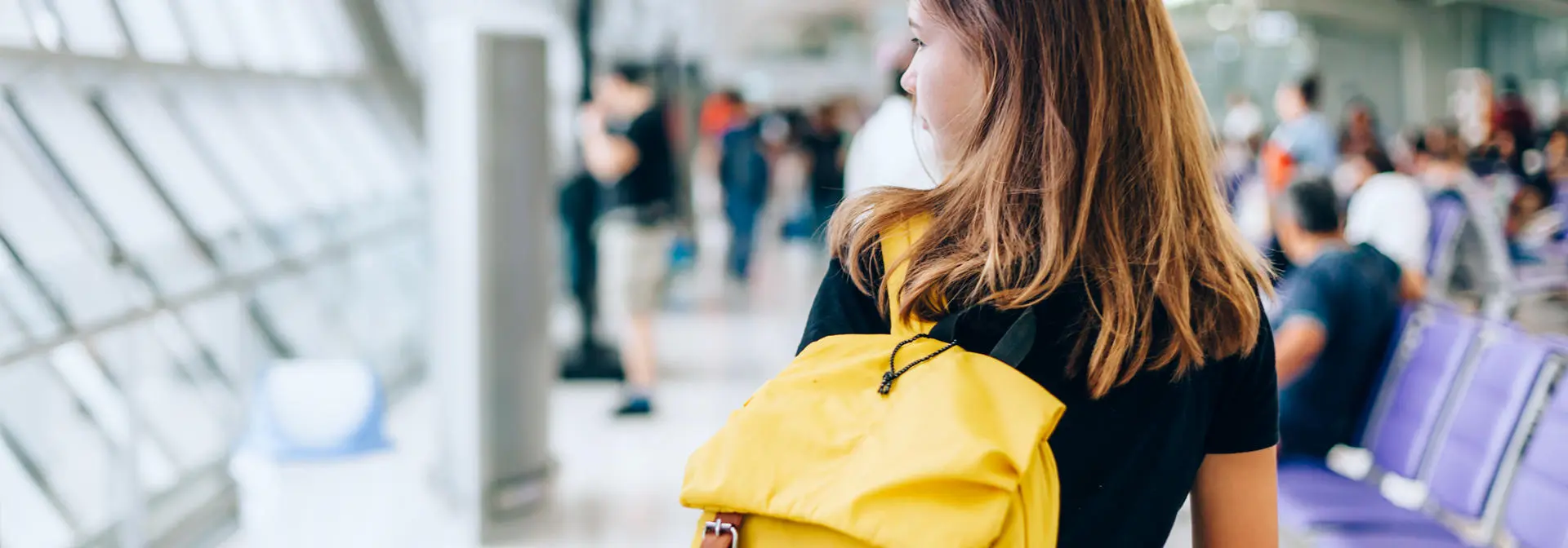 A student walking through the airport with yellow backpack.