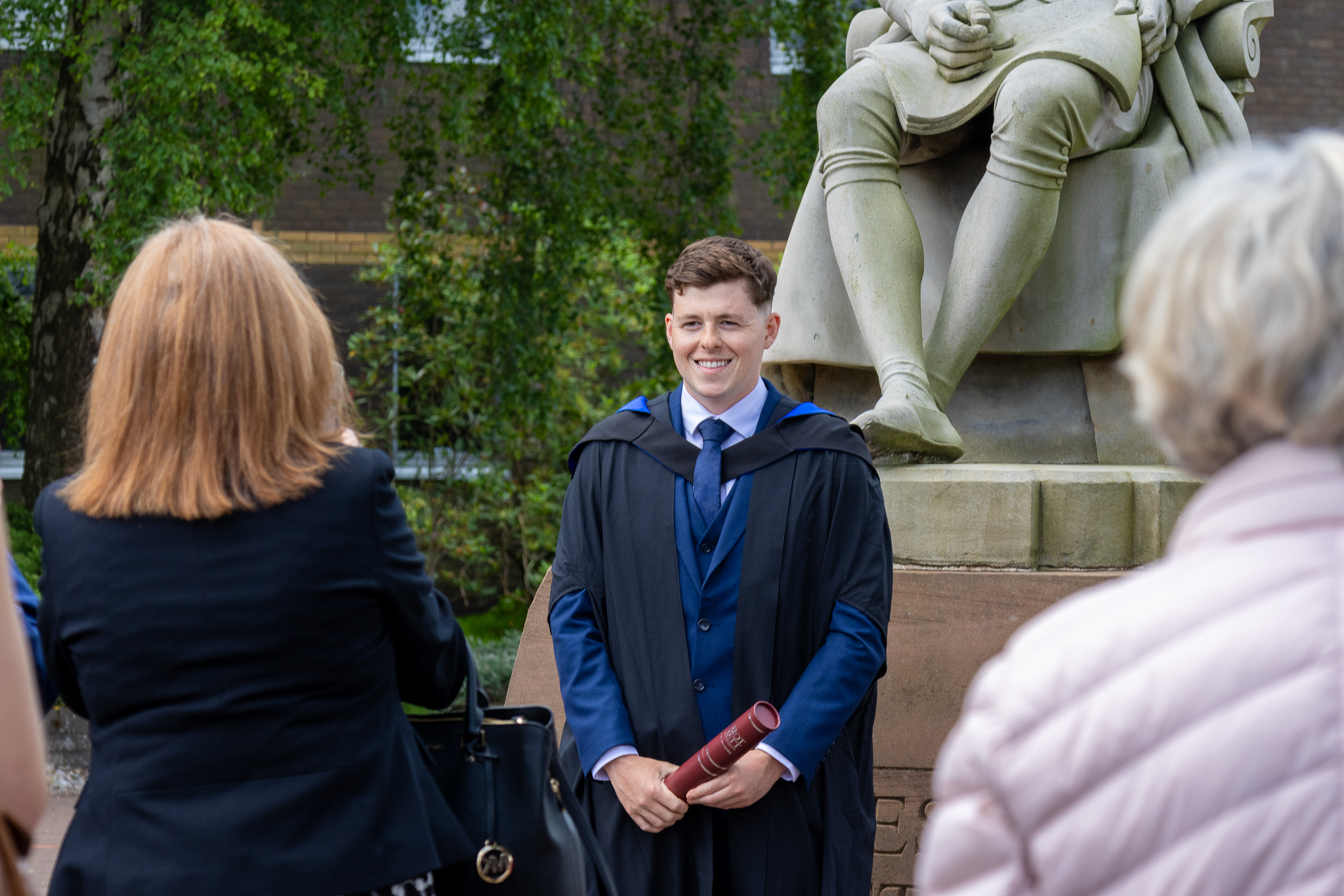 A graduate poses in front of the James Watt statue at graduation at the Edinburgh campus.