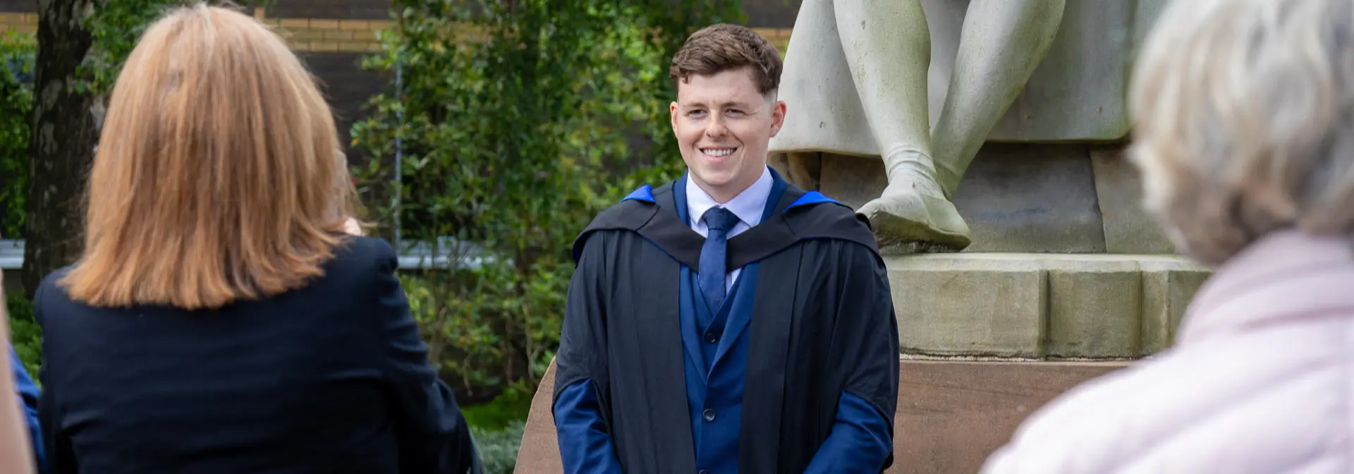 A graduate poses in front of the James Watt statue at graduation at the Edinburgh campus.