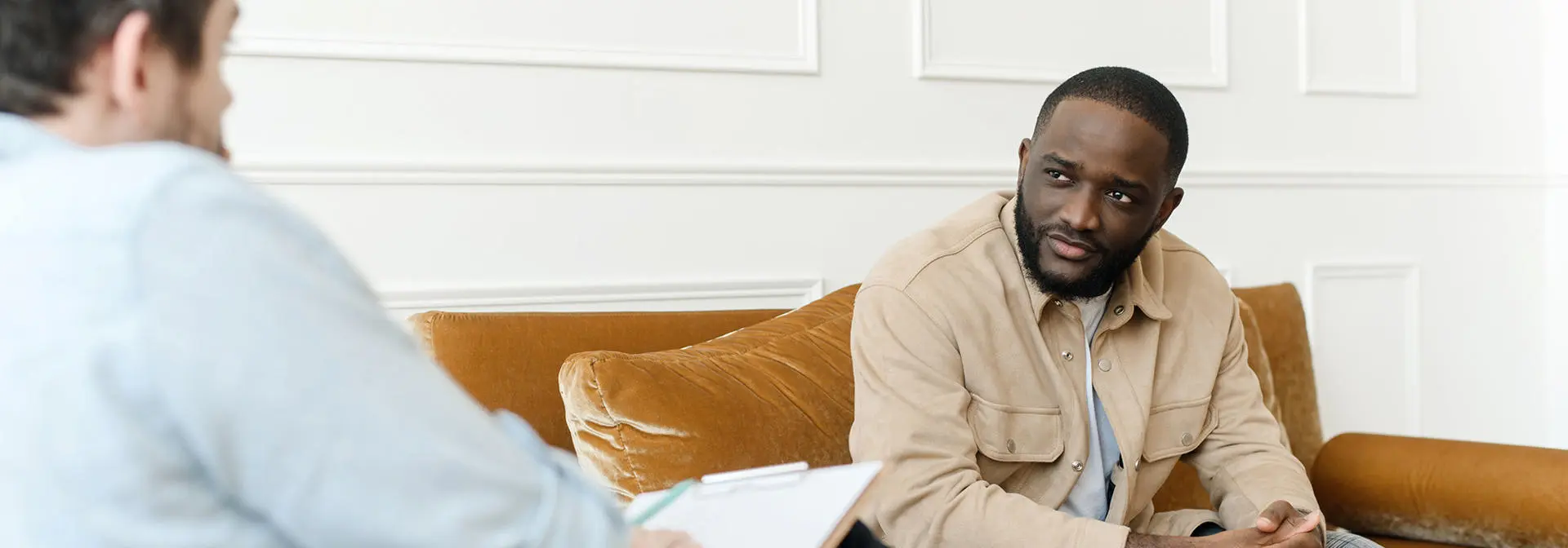 An individual sits on an orange sofa in a counselling session.