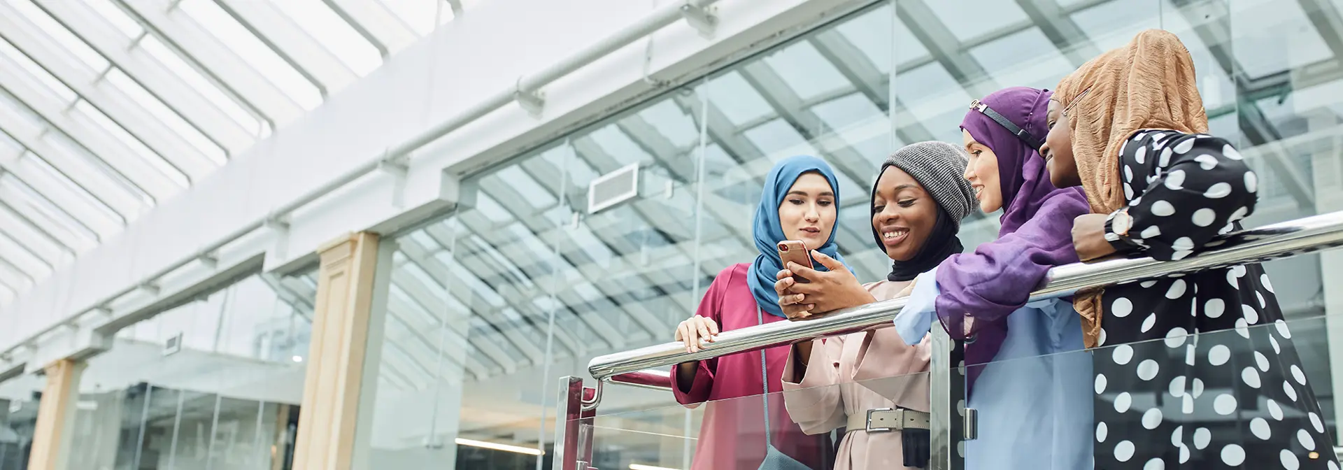 Four individuals stand looking at a phone on a balcony.
