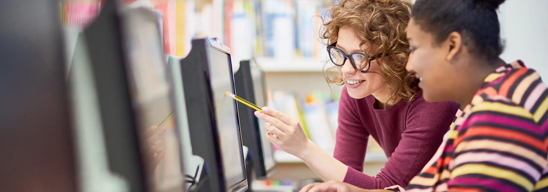 Two individuals working at a computer in a library.