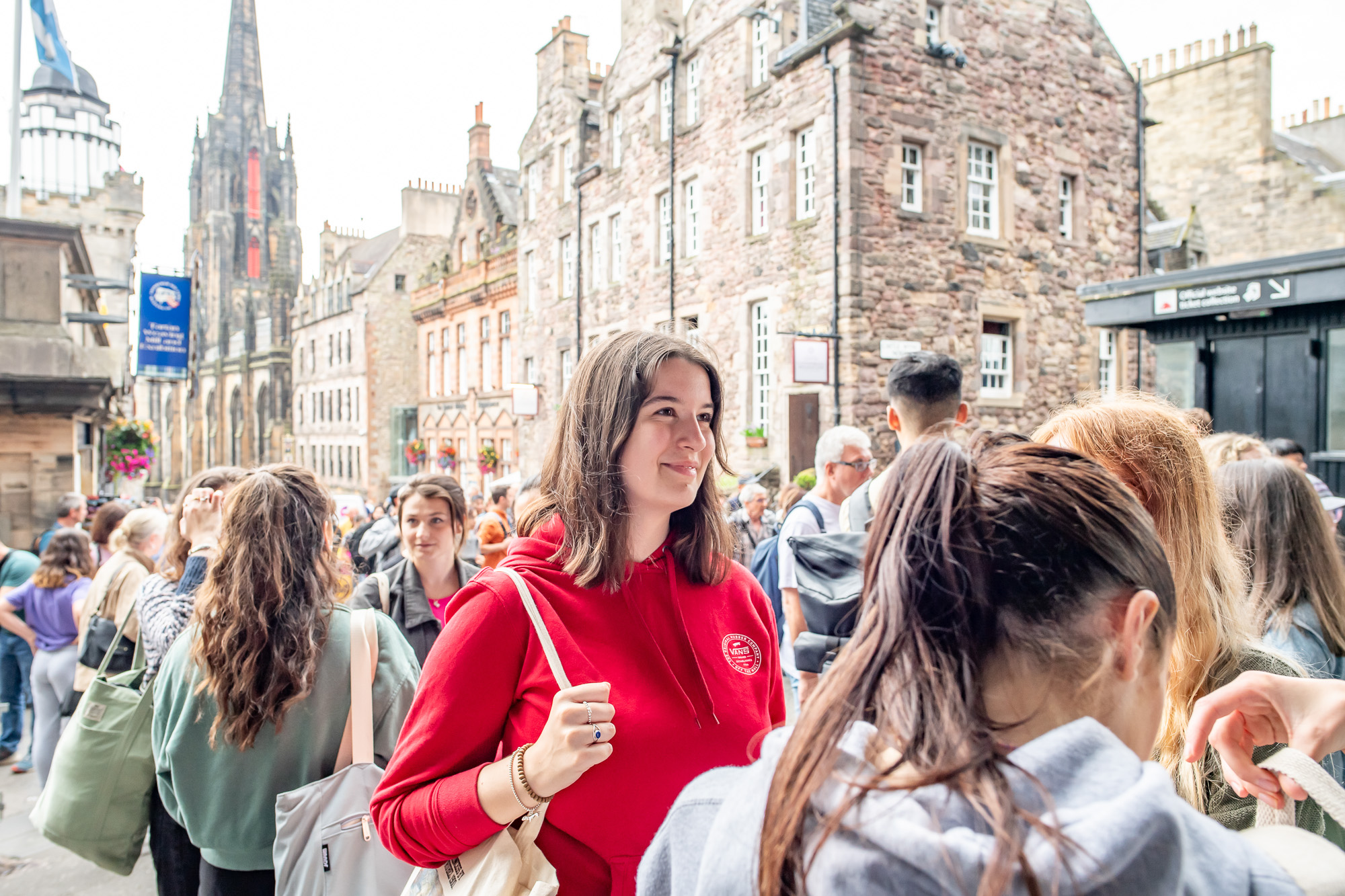 Student wearing a red hoodie and holding a canvas bag smiles in conversation.
