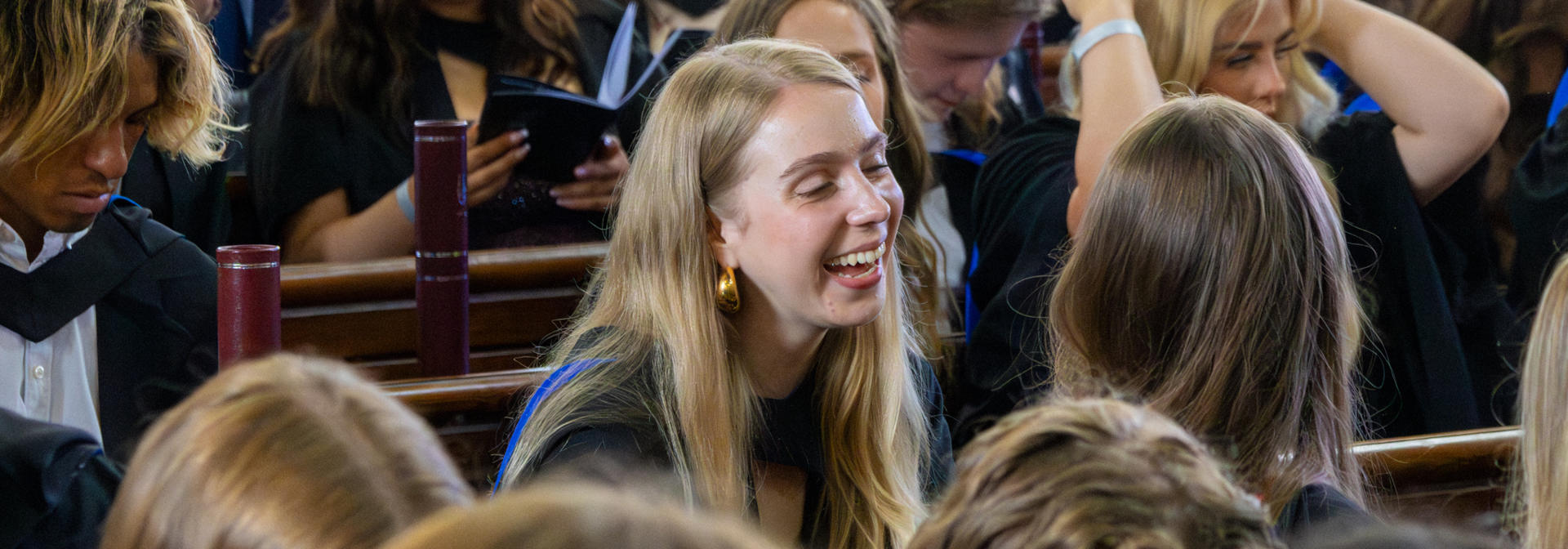 Students laughing in discussion as they sit in the graduation ceremony hall.