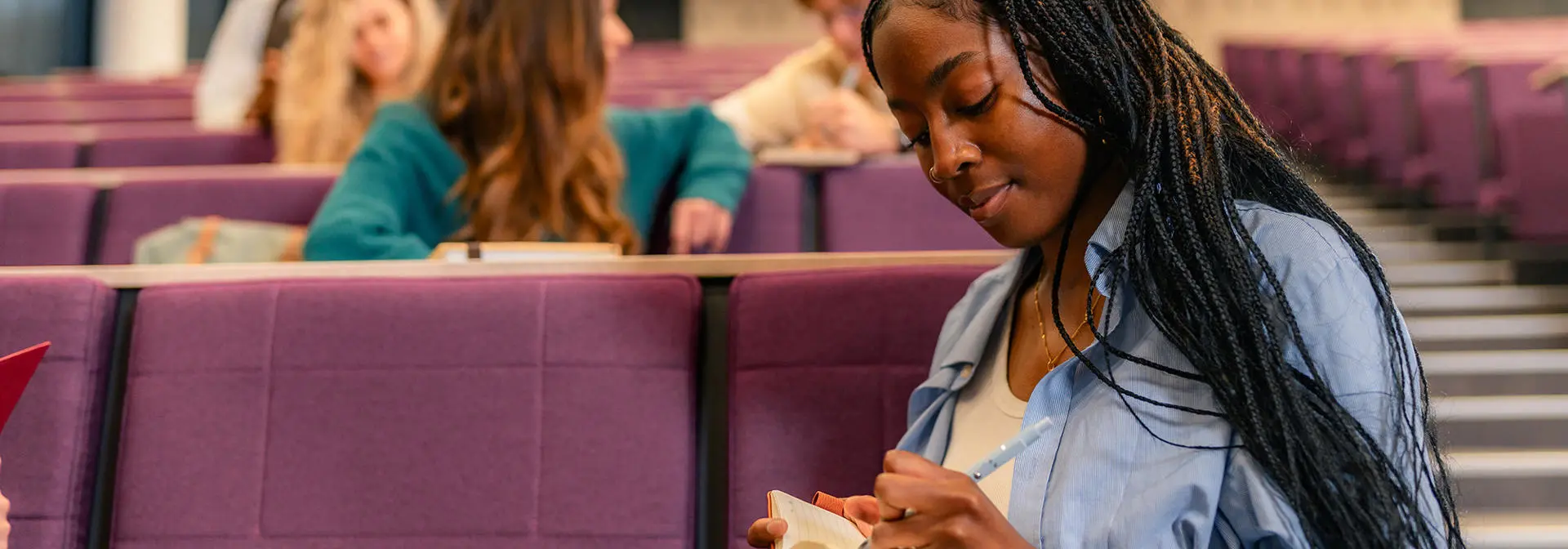 A student takes notes while sitting in a lecture hall.