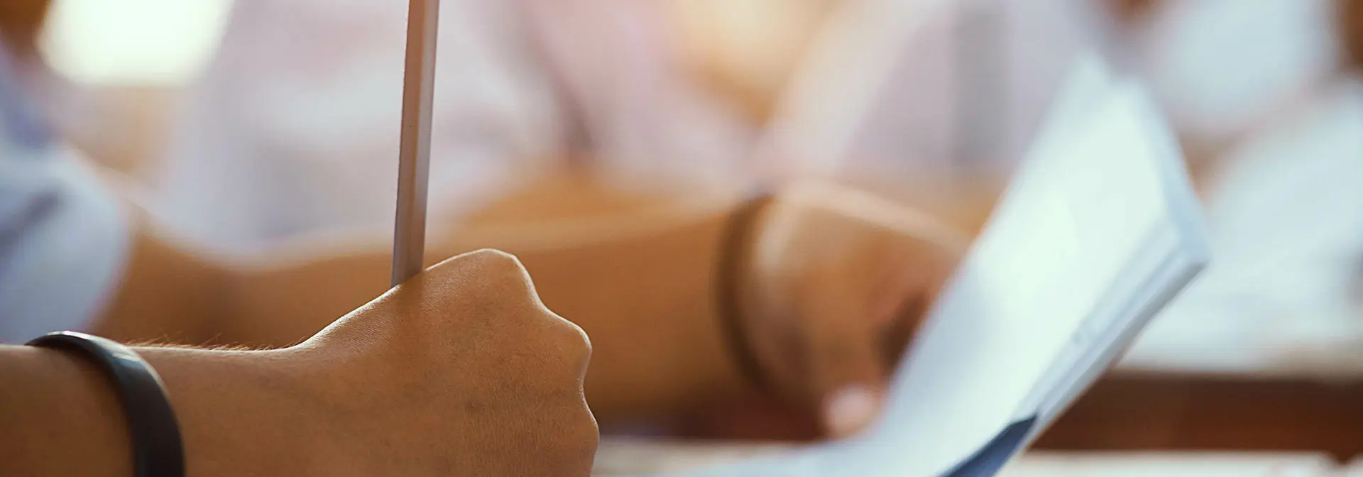 A student writing with a pencil on paper.