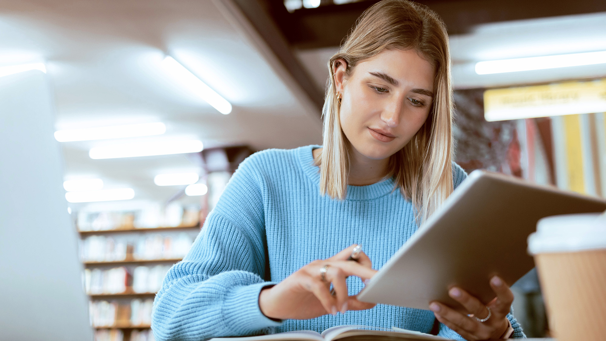 A student in the library checking work on a tablet.