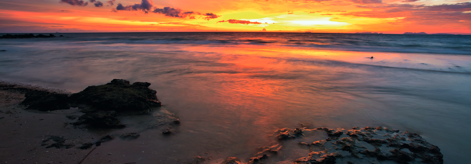 An orange sunset over the water at the beach.
