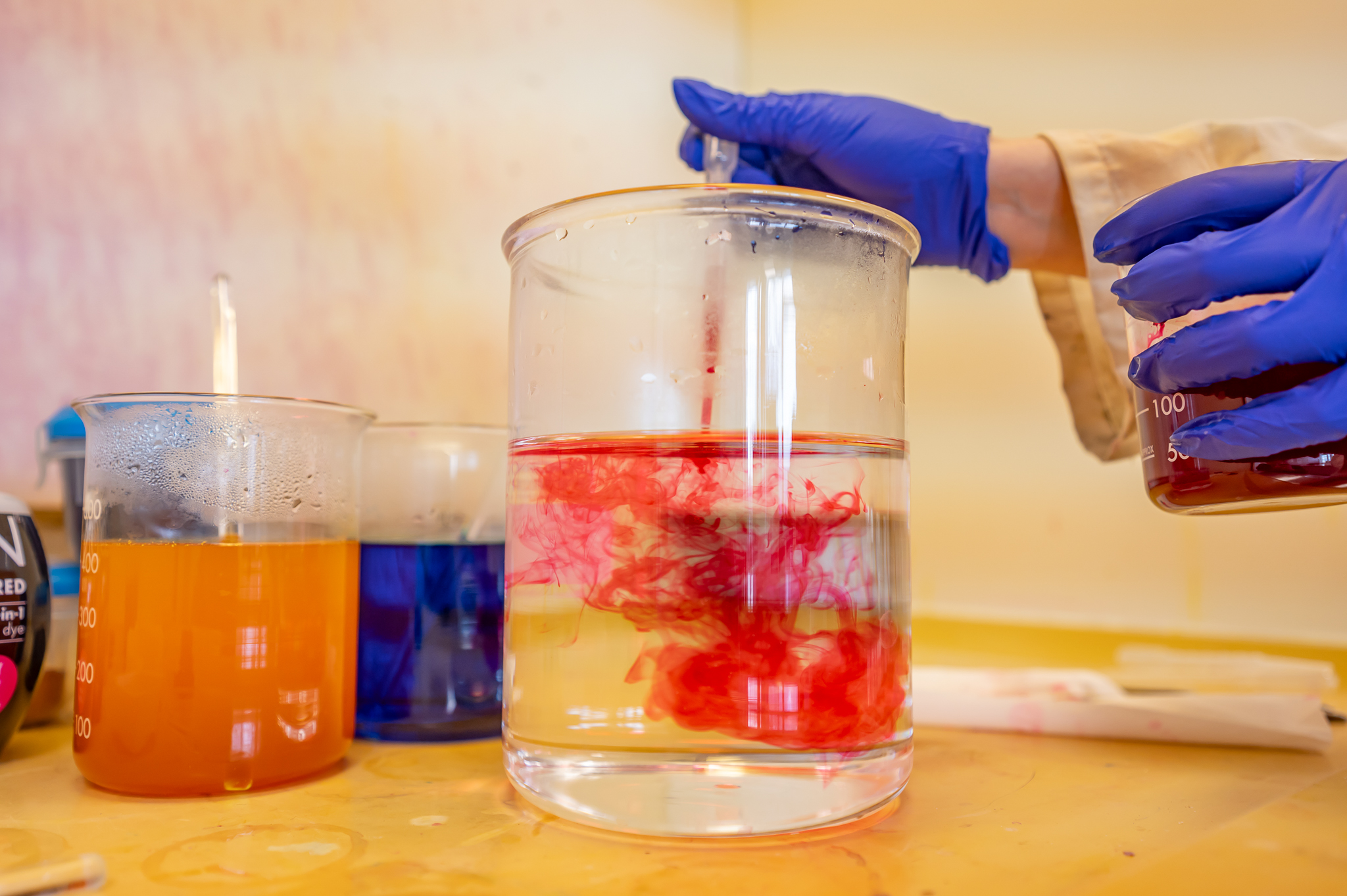 A person adds red dye to a beaker.