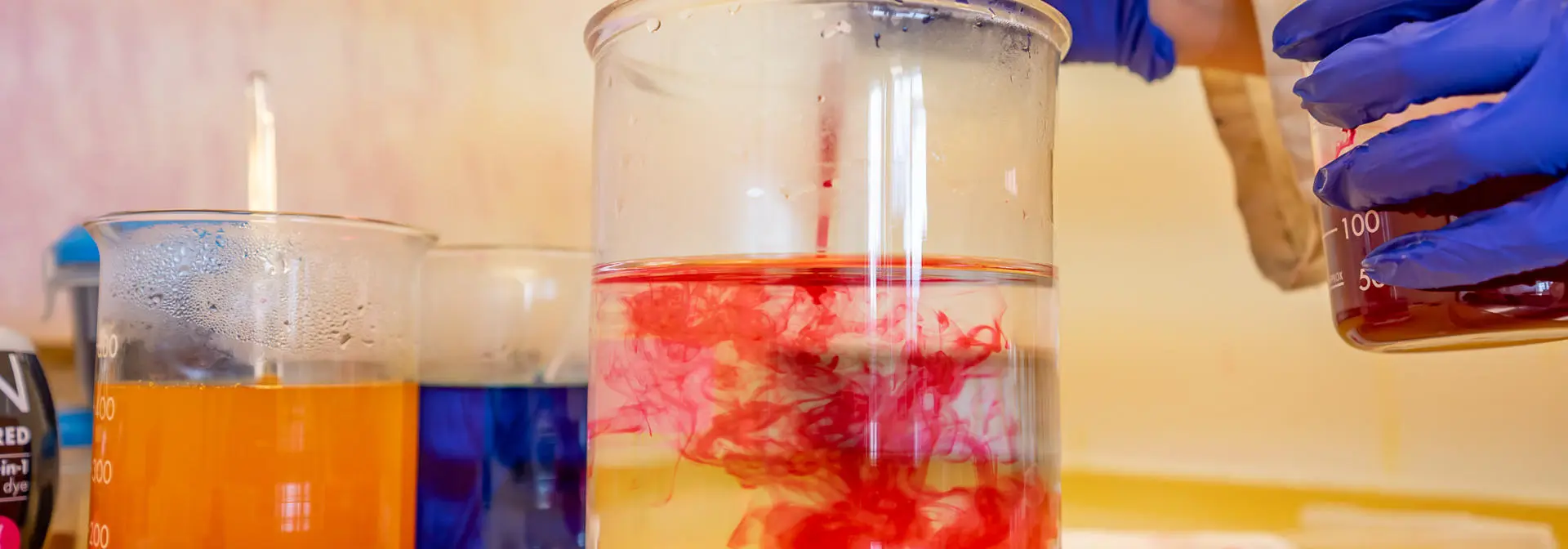 A person adds red dye to a beaker.