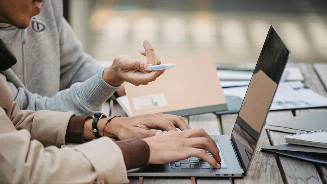 Two individuals working outside on a laptop.