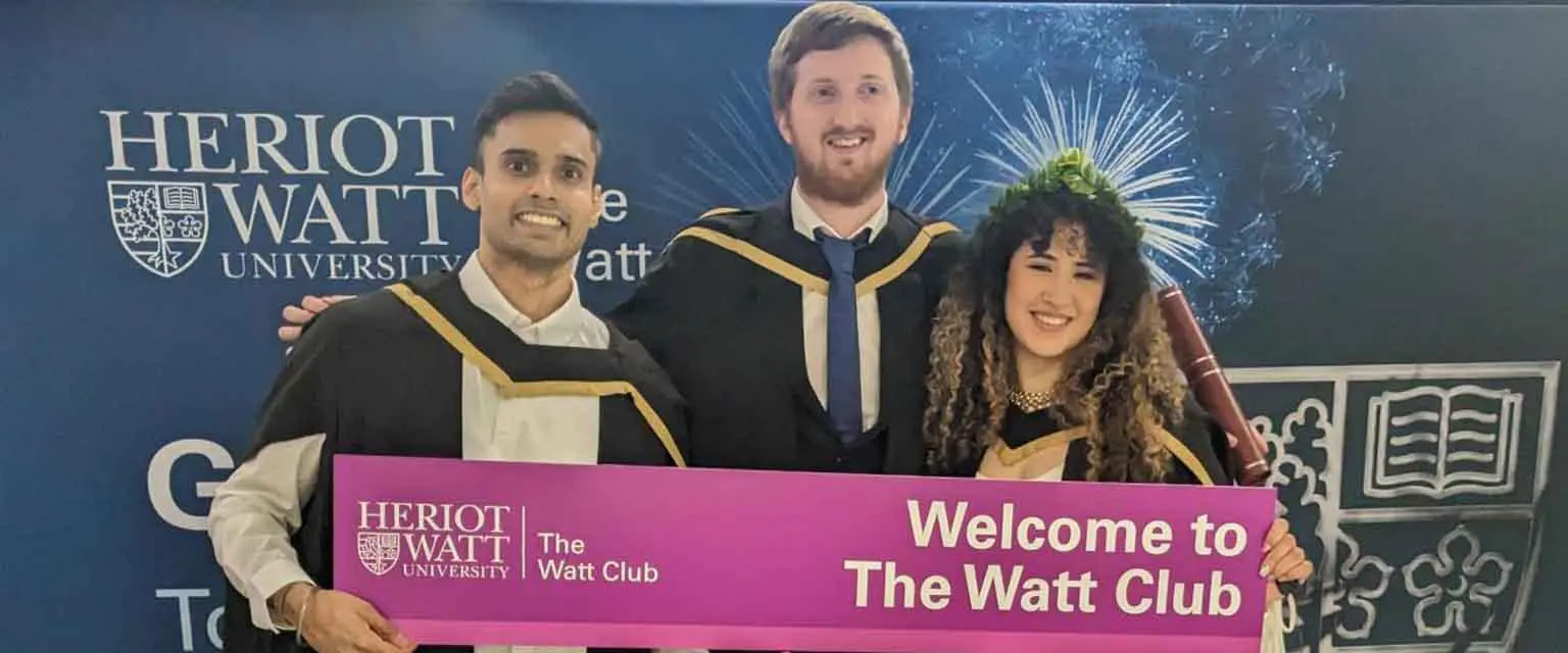 Three graduates in robes proudly hold a welcome sign, celebrating their achievement together.