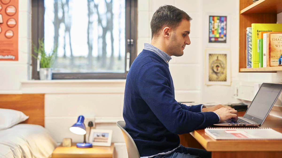 Male student sitting at the desk in student bedroom (traditional en suite room)