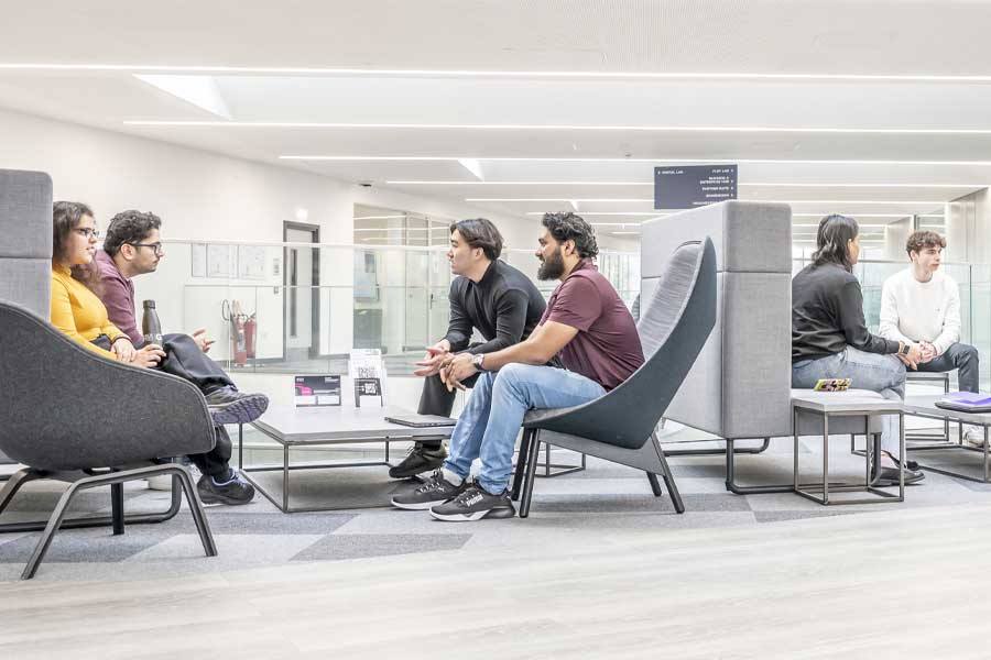 Two groups of students sitting in booths talking in a modern building.