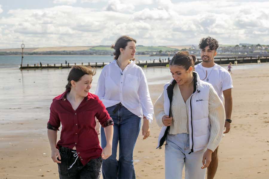 Four students stroll along the beach, enjoying the seaside scenery.