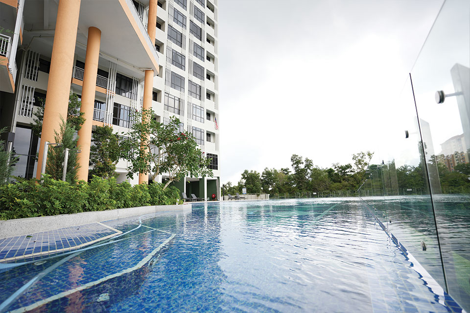 A serene swimming pool situated in front of a tall, modern building, reflecting the clear blue sky above.